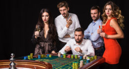Group of young people behind roulette table on black background