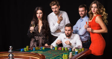 Group of young people behind roulette table on black background