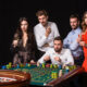 Group of young people behind roulette table on black background