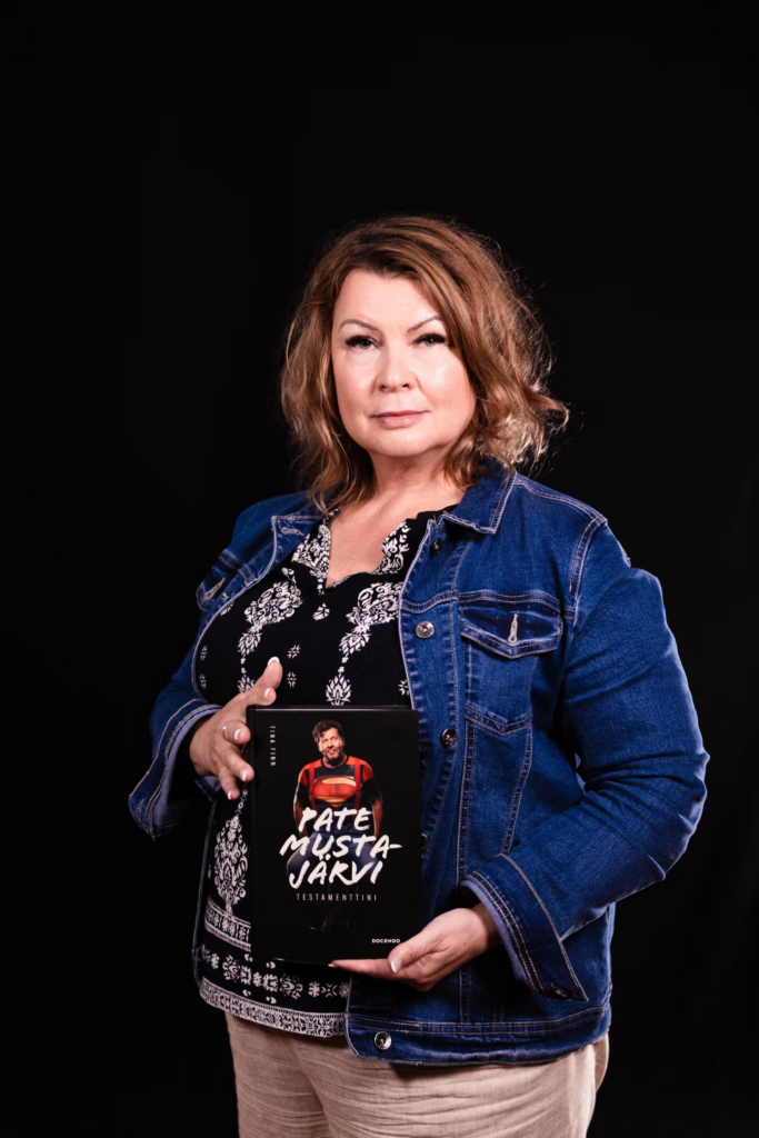 Tina Finn pitelee Pate Mustajärven Testamenttini-kirjaa
